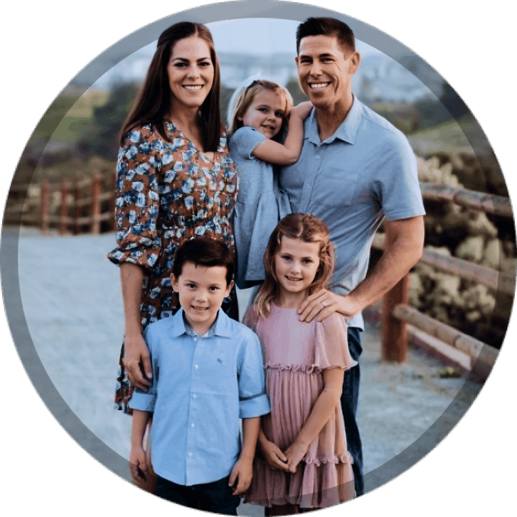 Family of five smiling together outdoors in casual clothing against natural landscape background.