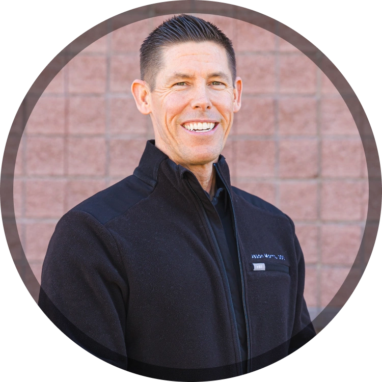 Professional headshot of smiling man in dark jacket against brick background for orthodontics practice.