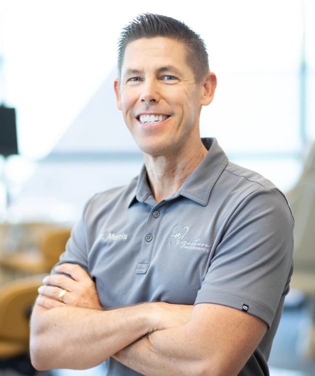 Professional man in gray shirt smiling with arms crossed in modern office setting.